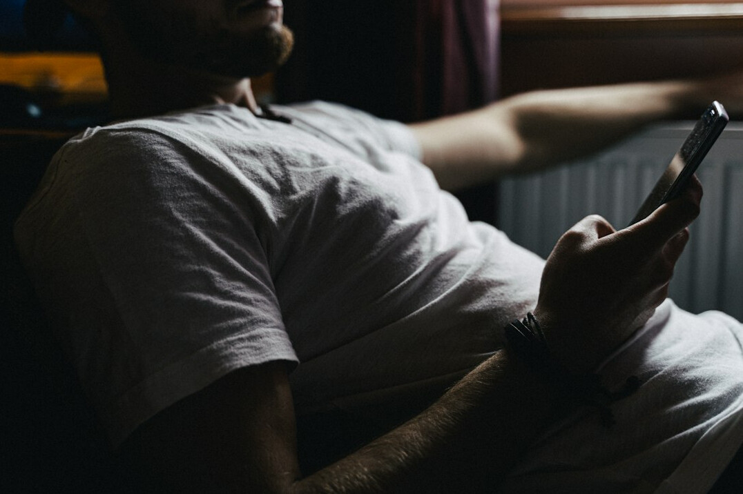 Brazilian man smiling while reading a message on his phone in a cozy home office